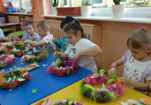 Dzieci ozdabiają wianek kolorową wstążką.