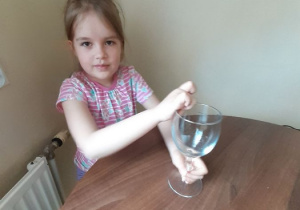 Zuzia trzyma w ręku puste naczynie szklane.