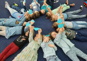 Dzieci leżą na dywanie z sercami w dłoniach.