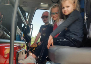 Dziewczynki siedzą w wozie strażackim.