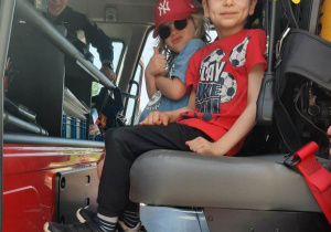 Chłopcy siedzą w wozie strażackim.