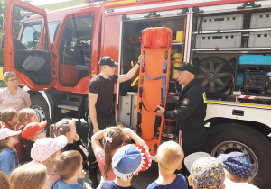 Strażacy tłumaczą do czego służą nosze będące na wyposażeniu wozu strażackiego.