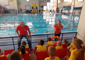 Dzieci poznają zasady bezpieczeństwa na basenie, o których mówi ratownik.